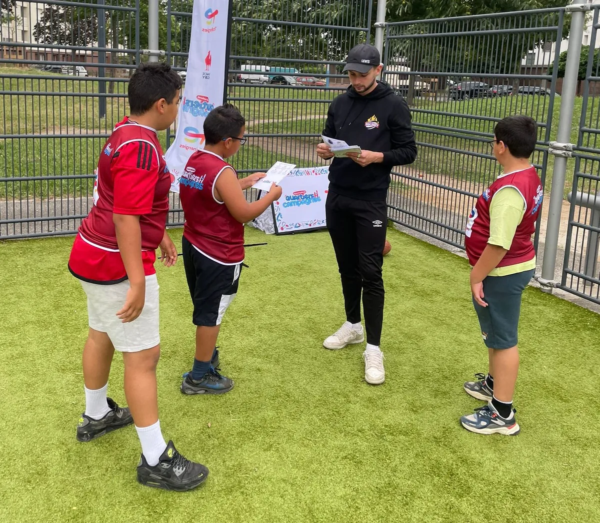 Un éducateur sportif encadre une séance d'initiation avec des enfants sur un terrain de quartier